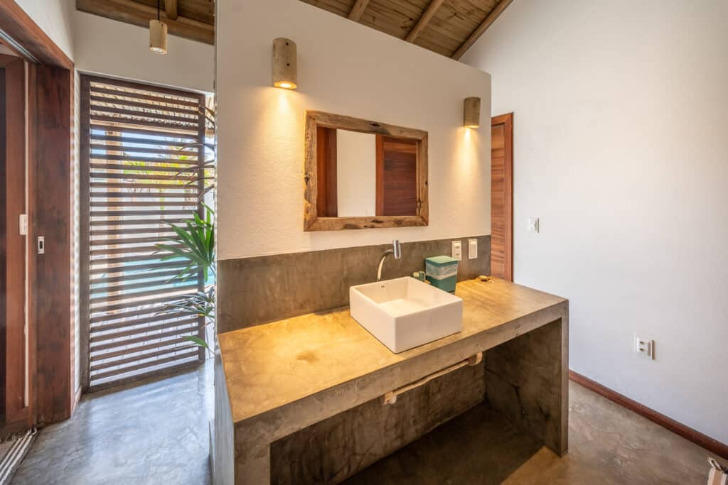 Salle de bain en béton ciré avec vasque blanche et miroir en bois, La Kite Family, Pontal de Maceió
