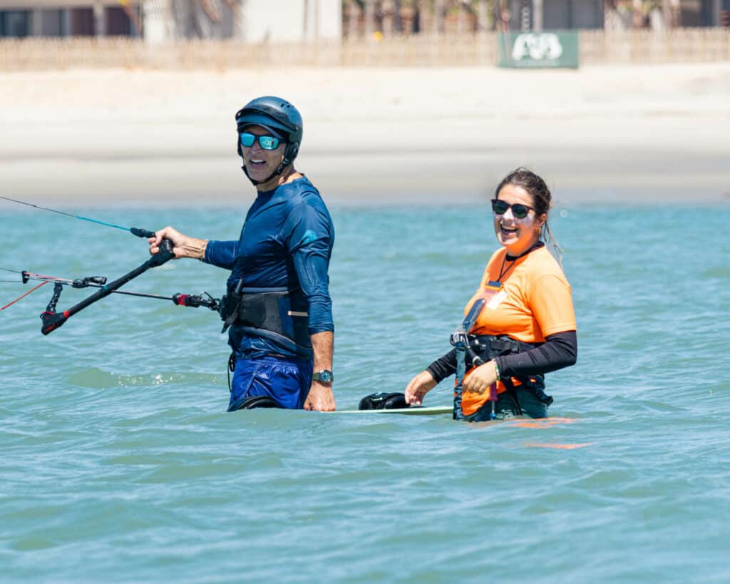 Monitrice et élève riant ensemble dans l'eau pendant un cours de kitesurf, One Launch Kite House, Pontal de Maceió