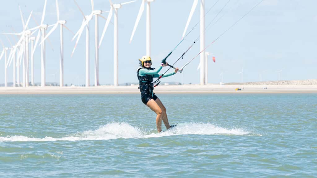 Kitesurfeuse naviguant devant des éoliennes avec casque jaune et harnais, spot de Pontal de Maceió