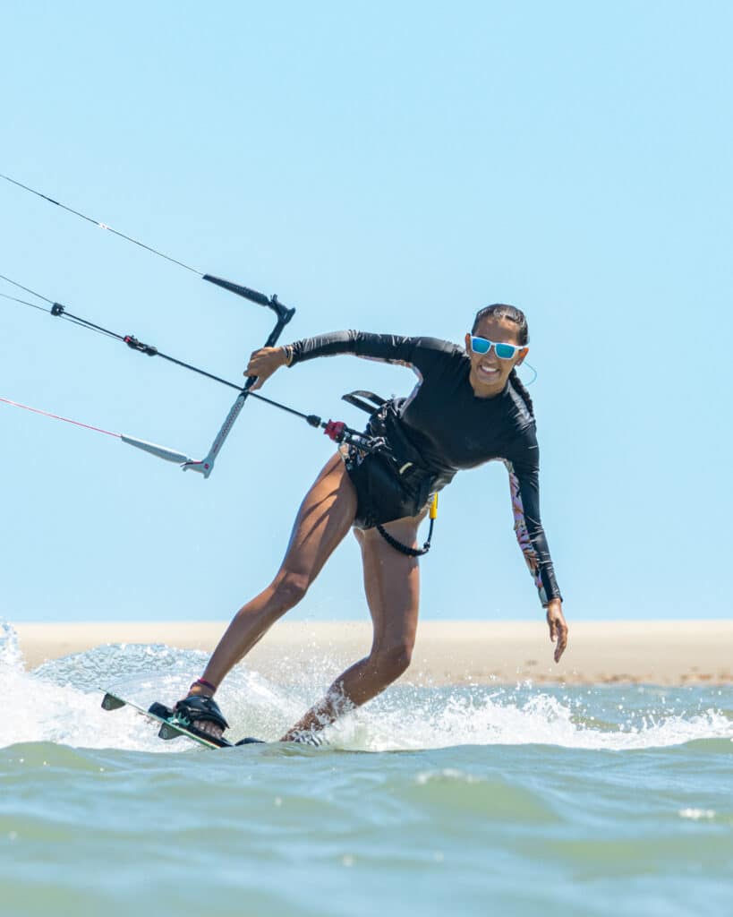 Kitesurfeuse en action sur sa planche avec barre en main et dunes en arrière-plan, Pontal de Maceió