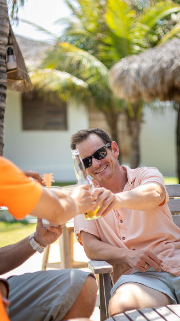Client trinquant avec une bière fraîche sous les palmiers au bar de la OLK House, Pontal de Maceió
