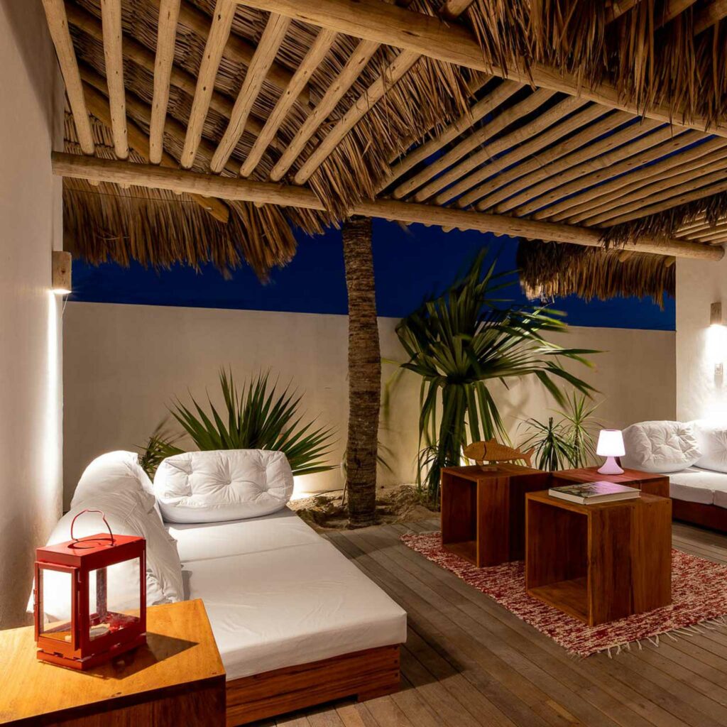 Espace détente nocturne avec coussins blancs, lanternes et palmiers sous toit en palme, One Launch Kite House, Fortim