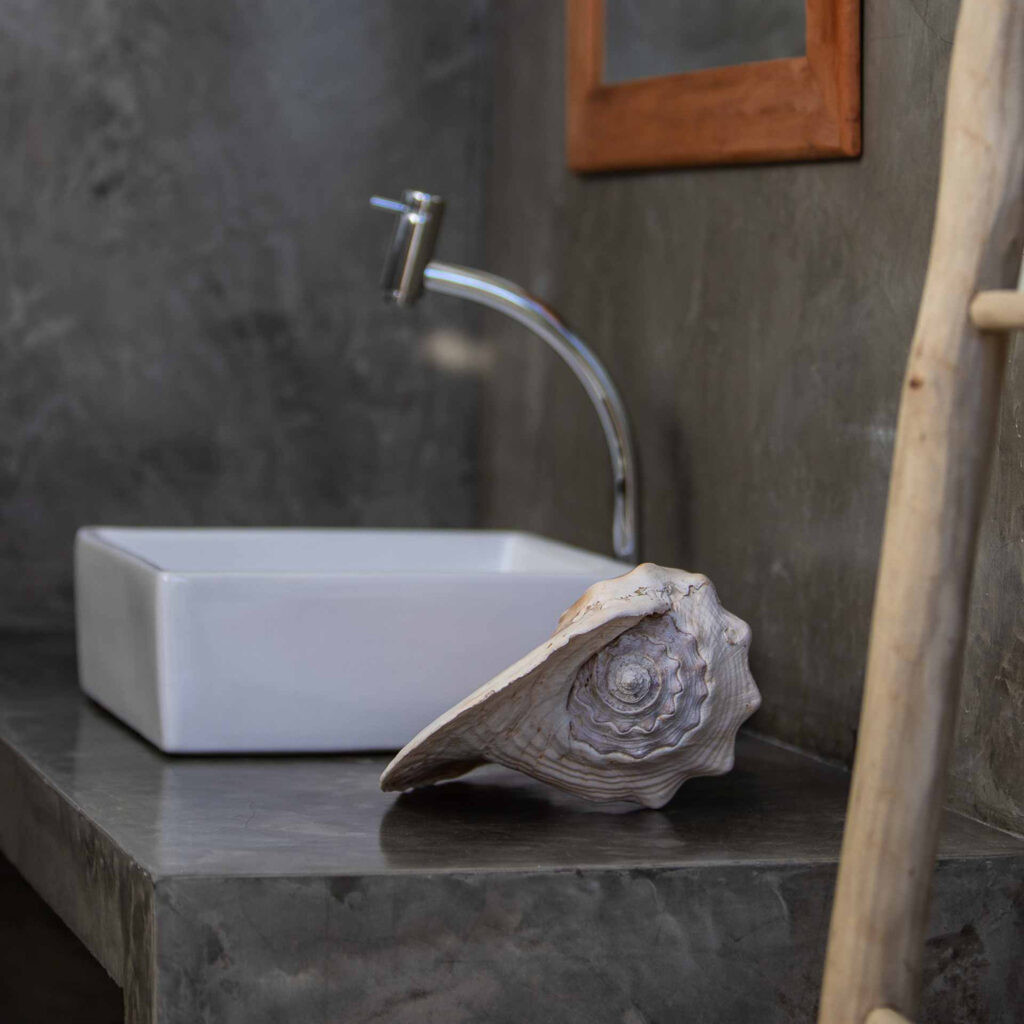 Salle de bain en béton ciré avec vasque blanche et coquillage décoratif, One Launch Kite House, Fortim